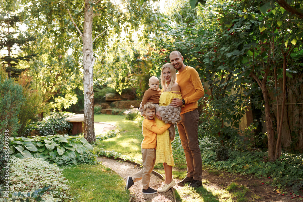 family in nature, summer or autumn, green grass trees in green leaves, a pond in nature, mom blonde in a yellow dress, dad, husband, older son and youngest son, two children, a large and happy family