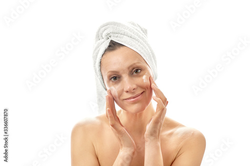 A young woman smears a white cream over her face with a large wipe. White isolated background.