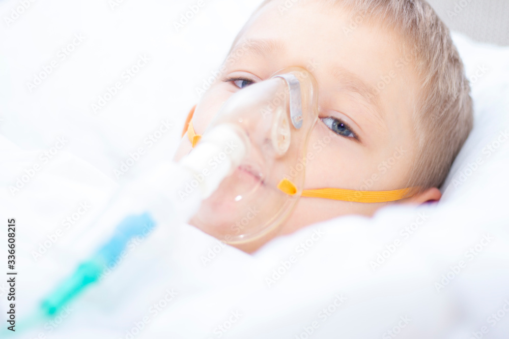 boy with an inhaler mask - respiratory problems in asthma. a boy with an inhaler mask lies in bed and breathes adrenaline. healthcare concept and sick child, coronavirus, bronchitis, pneumonia boy with an inhaler mask - respiratory problems in asthma. a boy with an inhaler mask lies in bed and breathes adrenaline. healthcare concept and sick child, coronavirus, bronchitis, pneumonia