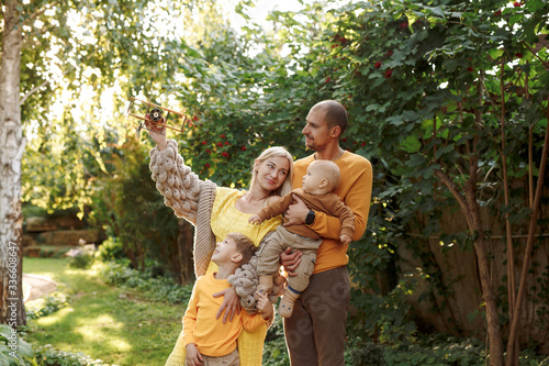 family in nature  summer or autumn  green grass trees in green leaves  a pond in nature  mom blonde in a yellow dress  dad  husband  older son and youngest son  two children  a large and happy family