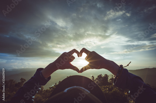 Woman making heart with her hands on sunset