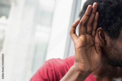 sad frustrated unhappy African black man listening ear to bad news or having hearing impair, hard of hearing; Concept of ear medication, hearing aid, rumor, fake news; African black man model photo