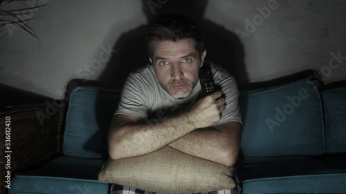 Quadro em tela young attractive concentrated and scared man holding TV remote watching horror m
