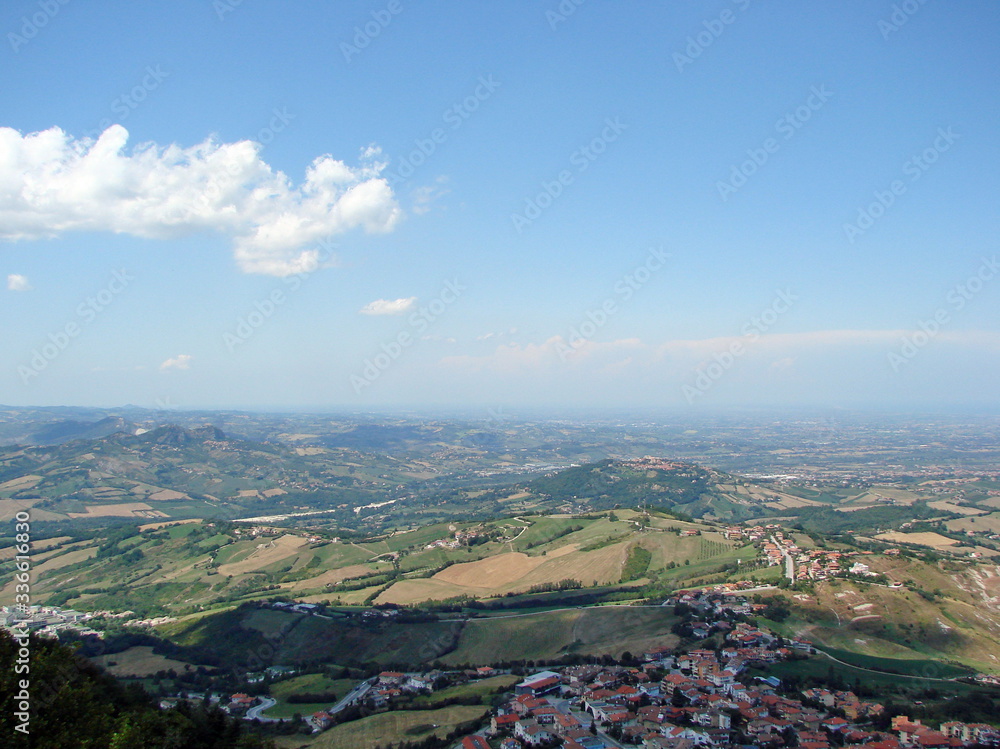 Panoramic view of mountain ranges on the horizon against the backdrop of sunny blue sky covered with lonely clouds.