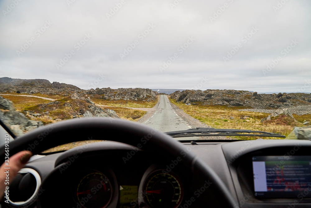 View from car window on the road and pity strange landscape with a mountains, rocks and cloudy sky and hand of woman. Landscape through windscreen in Norway