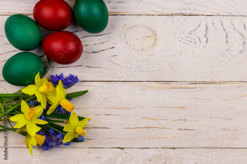 Painted Easter eggs and bouquet of yellow daffodils and blue scilla flowers on white wooden background. Easter composition. Top view, copy space