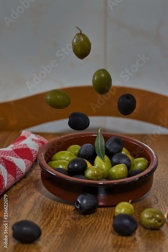 Fototapeta Naklejka Na Ścianę i Meble -  Green and black olives falling into a clay bowl
