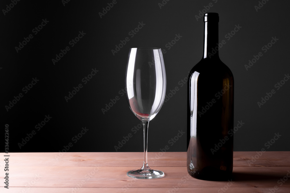 Black bottle of red wine and a glass. A bottle of wine stands on a table, a bottle on a gray background and a wooden table.