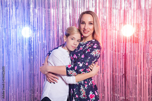 Mothers day, children and family concept - teen boy and his mom embracing on shiny party background.