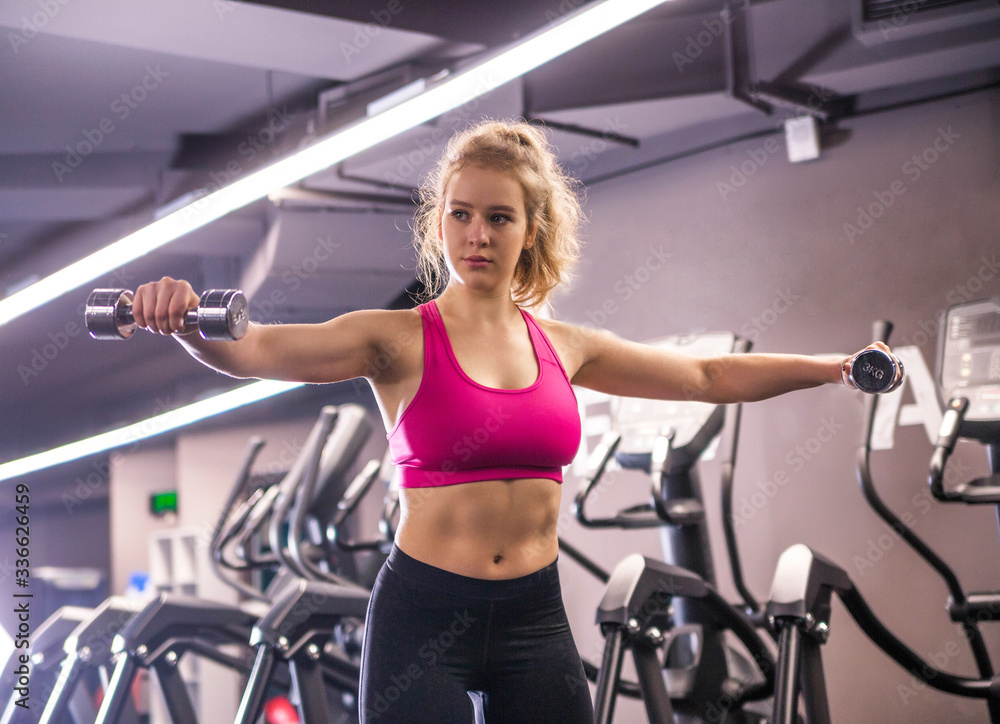 The girl does exercises with dumbbells in hands, trains hands in the gym The girl does exercises with dumbbells in hands, trains hands in the gym