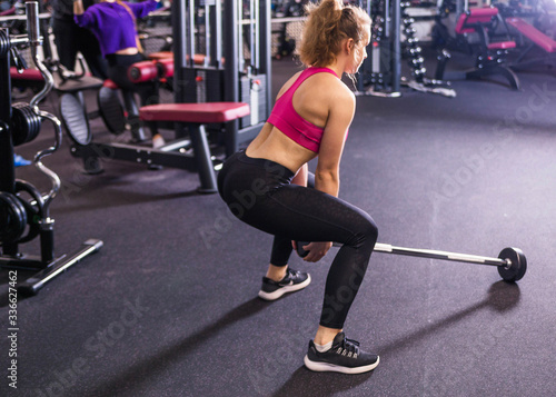 Attractive girl in black leggings and a pink top does squats with a barbell in her hands