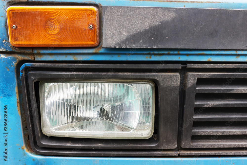 side lights of an old car are blue, of unknown make. An old battered car with traces of rust