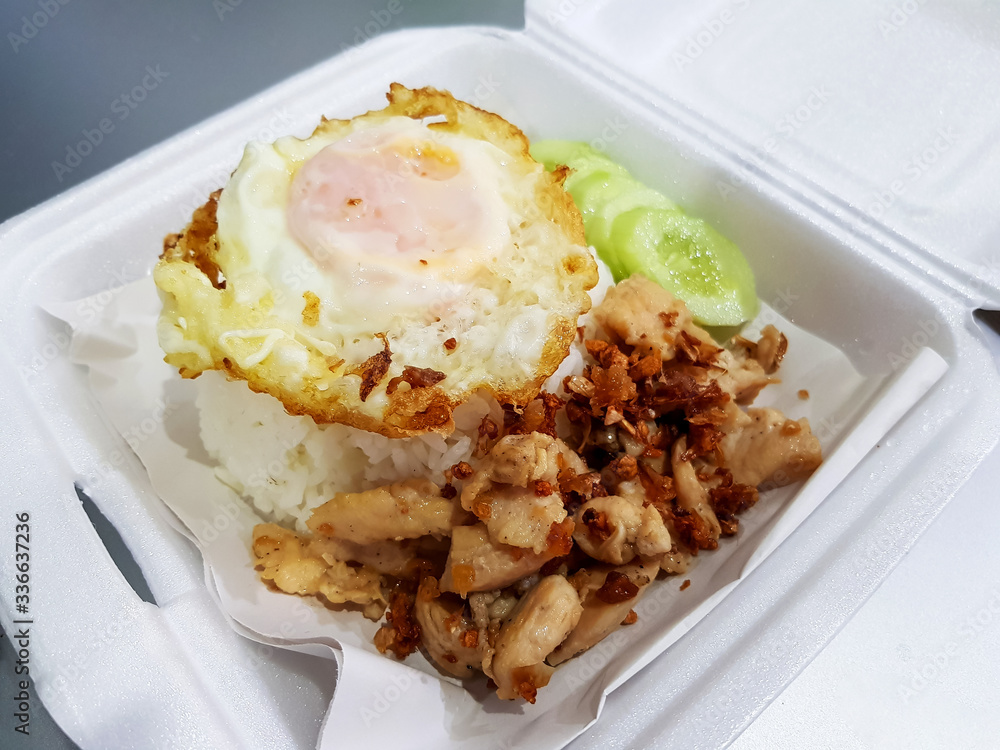 Garlic fried chicken topped with rice and a fried egg on paper for serving food in a foam box Garlic fried chicken topped with rice and a fried egg on paper for serving food in a foam box