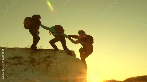 alpinists teamwork. Travel and adventure in mountains at sunset. team of climbers climbs a mountain holding out helping hand to each other. Free woman traveler climb mountain.