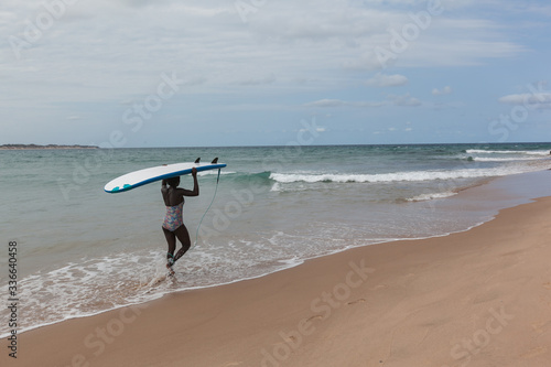 Beautiful young African surfer girl walking with surfboard to the ocean