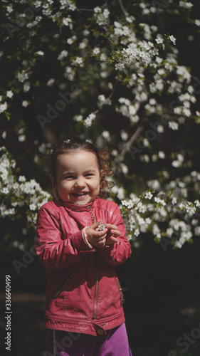Portrait of cute little girl among the branches of blossoming tree in spring