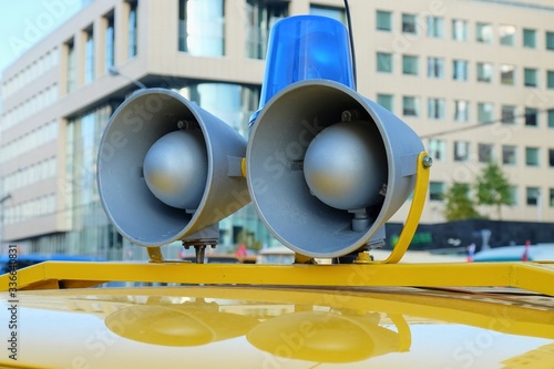 Details of retro police car with a megaphone and flashing blue siren light mounted on yellow top. Loud-hailers on police car for message information at emergency. Vintage loudspeakers.