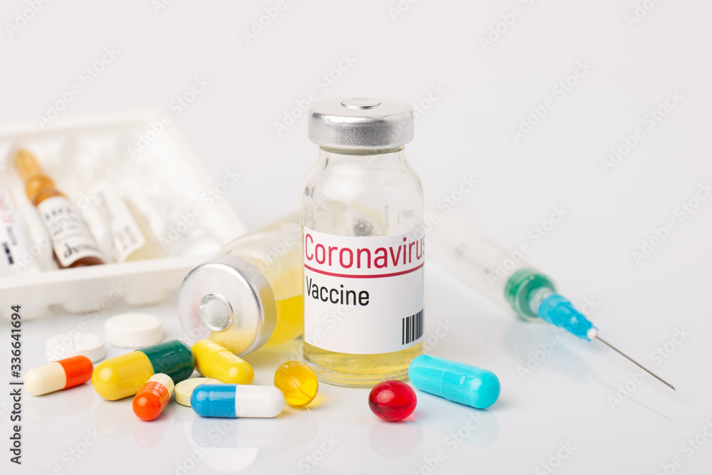 Concept of developing coronavirus vaccine. Two bottles with inscription Coronavirus vaccine, many pills and syringe on white table Concept of developing coronavirus vaccine. Two bottles with inscription Coronavirus vaccine, many pills and syringe on white table