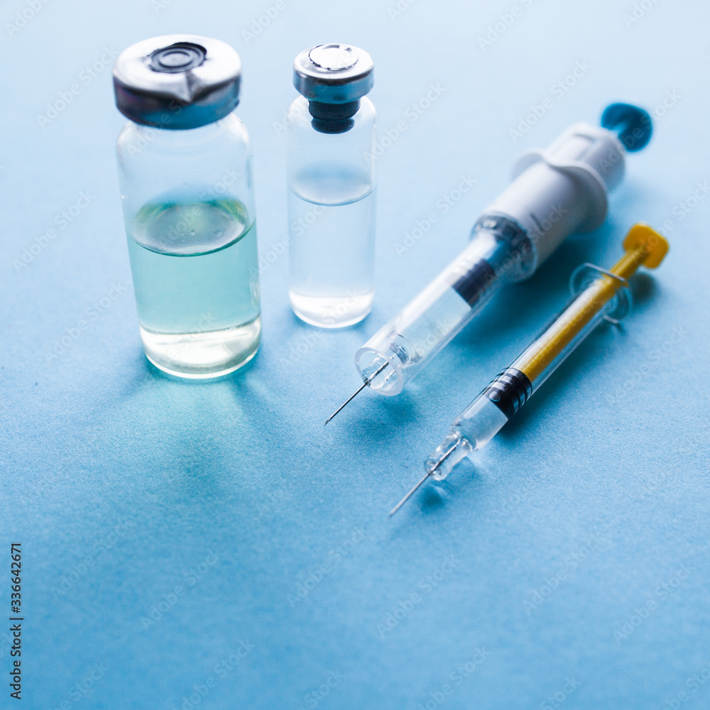 The covid-19 pandemic is concept. Vials of medication and syringe on a blue glass table with window background The covid-19 pandemic is concept. Vials of medication and syringe on a blue glass table with window background