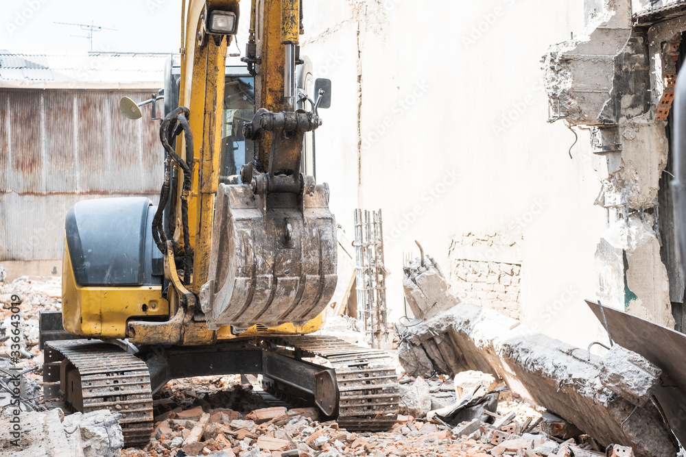 Small yellow excavator is on duty for pulling down the old buildings. Selective focus at bucket. Small yellow excavator is on duty for pulling down the old buildings. Selective focus at bucket.