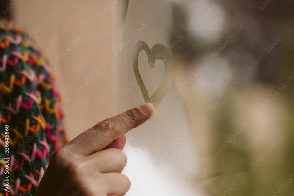 Young girl drawing hearts in the window. Love concept. 