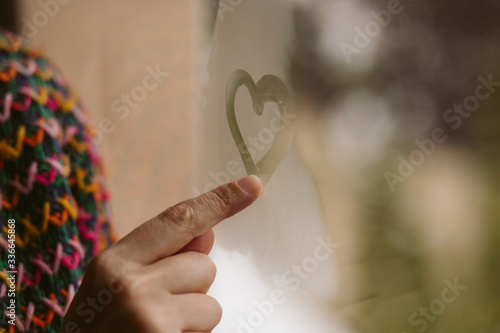 Young girl drawing hearts in the window. Love concept. 