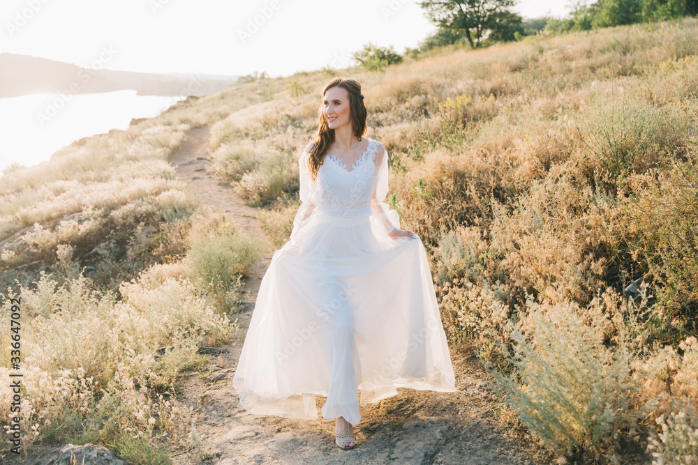 Bride in a luxurious white wedding dress in nature at sunset Bride in a luxurious white wedding dress in nature at sunset