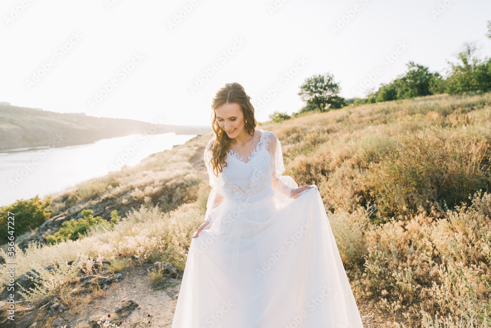 Bride in a luxurious white wedding dress in nature at sunset Bride in a luxurious white wedding dress in nature at sunset