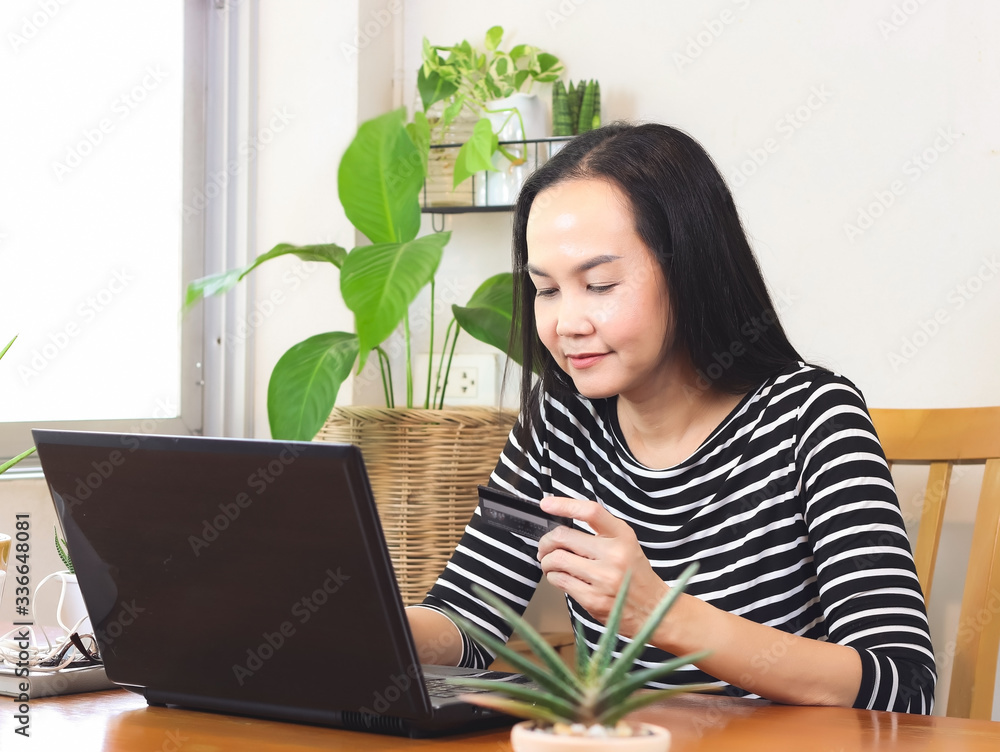 woman sitting at wooden table indoor holding credit card and typing on computer notebook on the table. Working at home and online shopping concept.