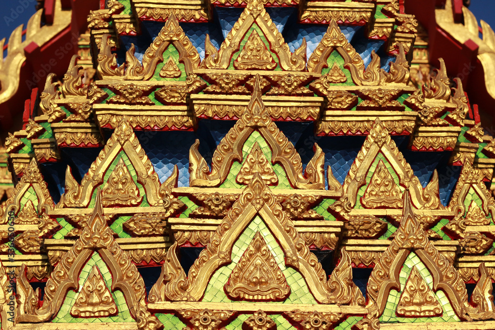 Close up detail of the ornate decoration on a Buddhist Thai temple roof with rows of small Buddha icon designs in gold