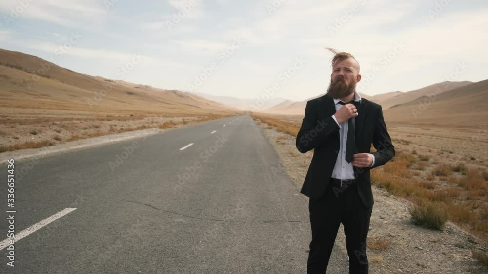 Caucasian man with a beard and mustache in a black suit with a tie and a white shirt, office worker happy excited waiting, trying to stop the car on an empty scenic mountain road 4k Caucasian man with a beard and mustache in a black suit with a tie and a white shirt, office worker happy excited waiting, trying to stop the car on an empty scenic mountain road 4k