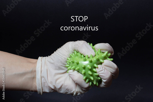 Hand in a medical glove tightly compresses a coronavirus on a black background. Close up