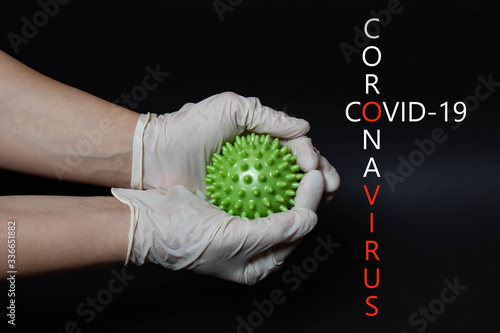 Pandemic. Hands in medical gloves hold coronavirus on black background. Macro