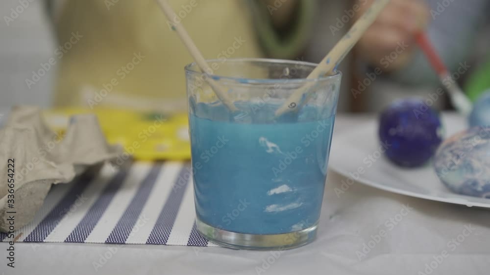 a glass of colored water. Children on the background paint an egg. Easter a glass of colored water. Children on the background paint an egg. Easter