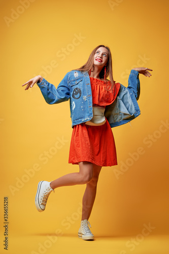 Summer urban fashion. Fun and colorful. Young pretty happy woman in orange dress posing against yellow background.