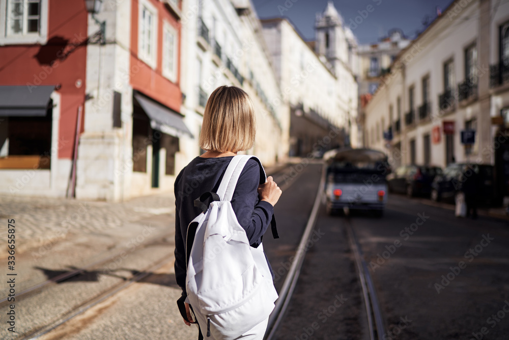 Traveling by Portugal. Happy young woman with rucksack walking by streets in Lisbon.