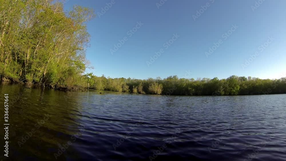 Boat-mounted forward trucking shot advances through rippling water towards wooded shoreline. Boat-mounted forward trucking shot advances through rippling water towards wooded shoreline.