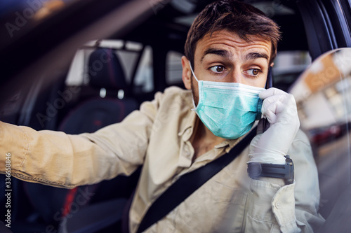 Man with protective mask and gloves driving a car talking on mobile phone smartphone. Infection prevention and control of epidemic. World pandemic. Stay safe.