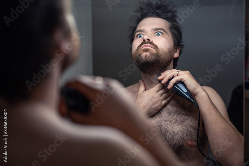 man shaves his beard in the reflection of the mirror