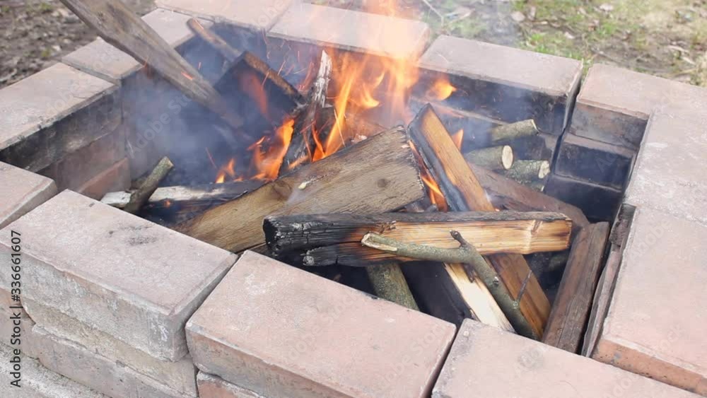 firewood is burning inside the grill made of stones. A man puts new branches and planks, a lot of smoke because of the wind. Air pollution due to burning firewood is burning inside the grill made of stones. A man puts new branches and planks, a lot of smoke because of the wind. Air pollution due to burning