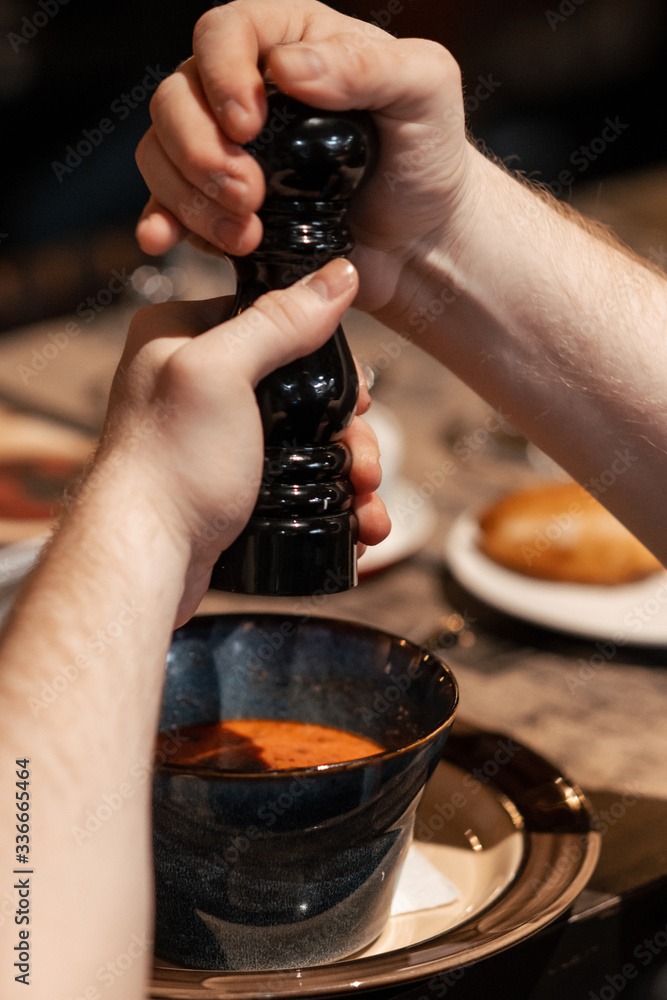 hands hold pepper shaker and add spices to soup. Close-up.