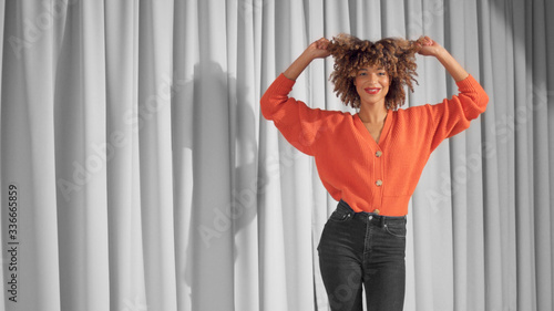 Mixed race black woman with curly hair and natural warm make-up for dark skin dancing and touching her hair