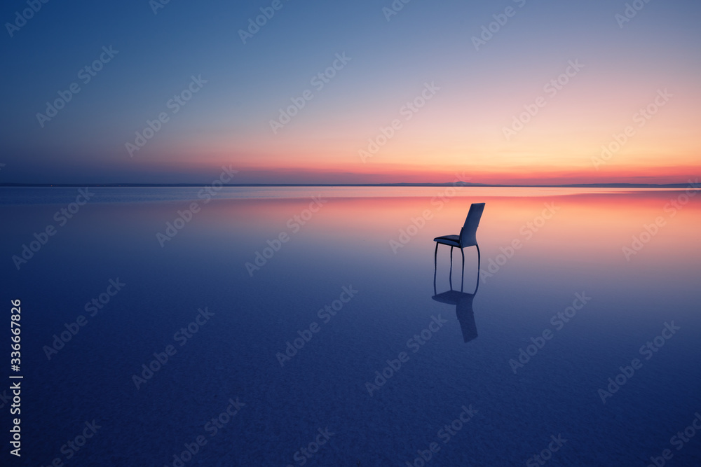 Chair among smooth water of lake at sunset