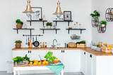 White Kitchen, Colorful Fruits and Vegetables on White Table and Wooden Counter, Pots, Plates, Boxes and Plants and kitchen accessoires on Shelves.