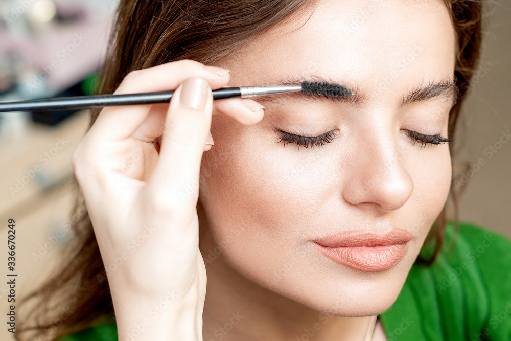 Makeup artist combs eyebrows with eyebrow brush tool. Makeup artist combs eyebrows with eyebrow brush tool.