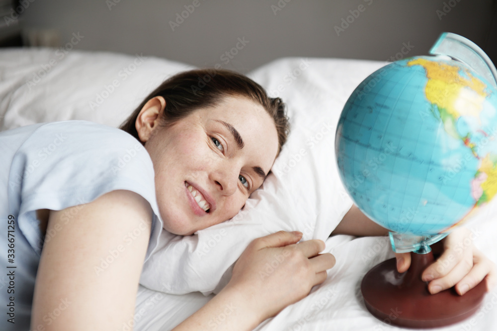 Beautiful woman dreaming about vacation. Girl holds in hand a small globe and laying in the bed. Beautiful woman dreaming about vacation. Girl holds in hand a small globe and laying in the bed.