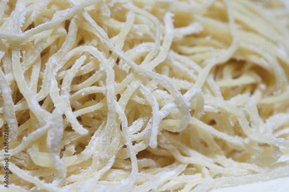 Closeup of raw fresh yellow egg noodles mixed with white powder in the kitchen for traditional Asian food preparation and cooking concept