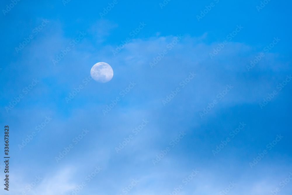 Blue sky surrounded by diffuse clouds and the Earth`s natural satellite, the Moon, in the background Blue sky surrounded by diffuse clouds and the Earth`s natural satellite, the Moon, in the background