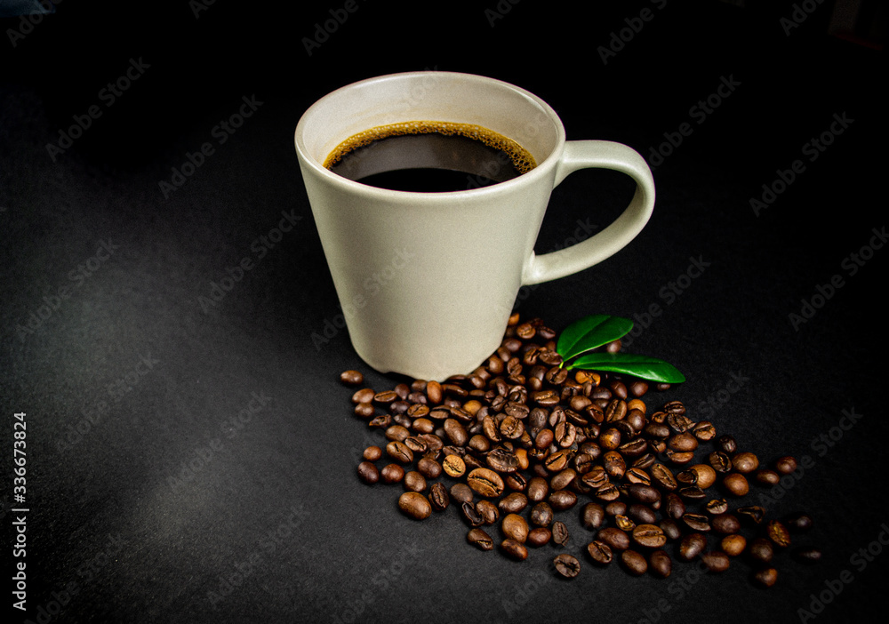 Cup of coffee with roasted beans and green leaves on black background Cup of coffee with roasted beans and green leaves on black background