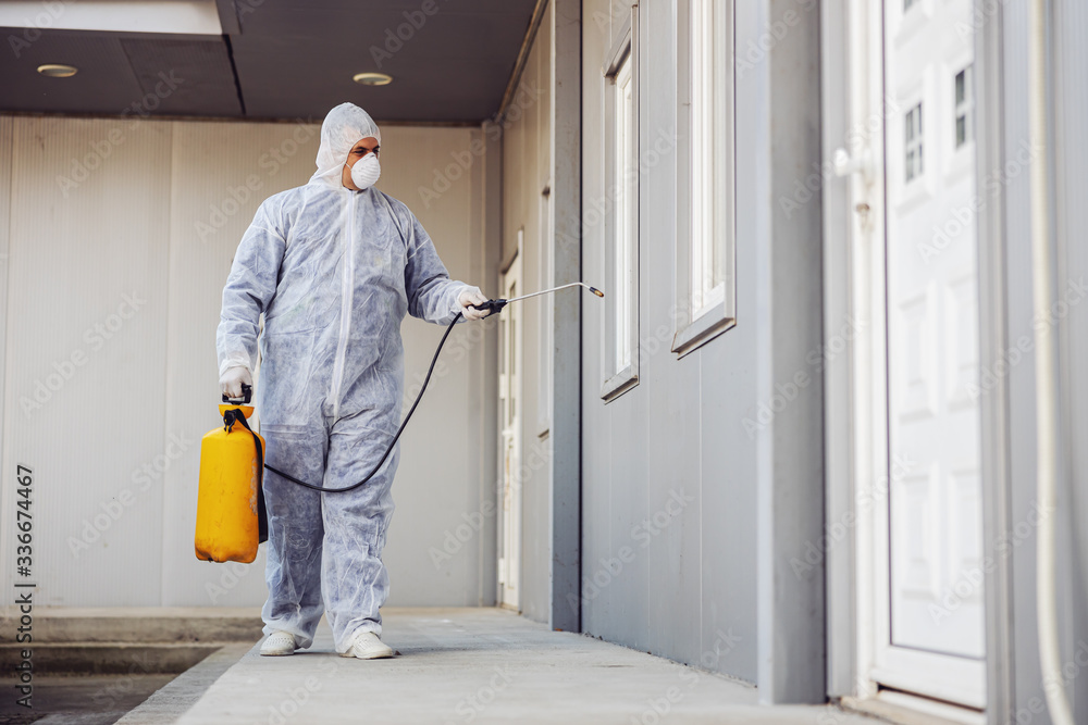 Man in virus protective suit and mask disinfecting buildings of coronavirus with the sprayer. Infection prevention and control of epidemic. World pandemic.